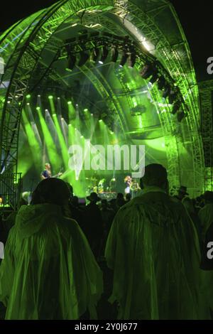 Pubblico in poncho antipioggia a un concerto serale di fronte a un palcoscenico illuminato da verde, Klostersommer, Calw Hirsau, Foresta Nera, Germania, Europa Foto Stock