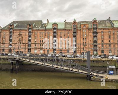 Lunga fila di edifici in mattoni vicino a un canale, sopra un ponte di metallo, automobili e un cielo nuvoloso, Amburgo, Germania, Europa Foto Stock