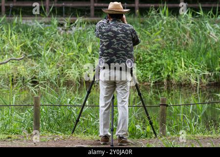 Un fotografo che indossa una giacca camuffata Kuchofuku con aria condizionata scatta foto utilizzando un treppiede in un parco di Kanagawa, Giappone. Foto Stock