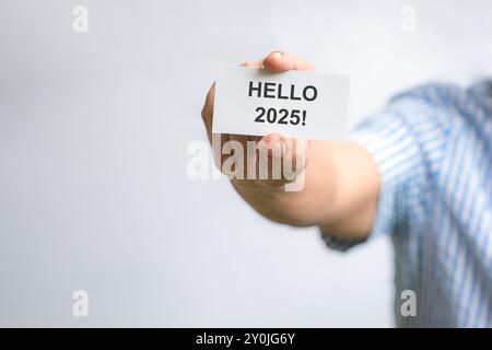 Uomo con un cartellino bianco con Hello 2025. Su sfondo bianco, copiare lo spazio. Foto Stock