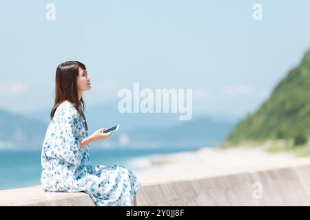 Donna con smartphone seduto su Breakwater Foto Stock