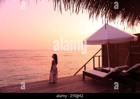 Ragazza che guarda il tramonto da un cottage delle Maldive Foto Stock