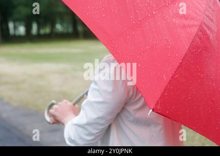 Donna che indossa un ombrello rosso in un giorno di pioggia Foto Stock