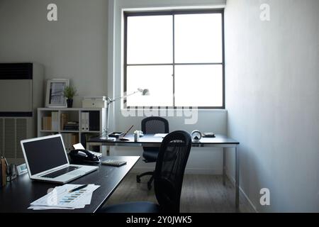 Due scrivanie posizionate vicino alla finestra e ai documenti e un personal computer sulla scrivania della libreria in una stanza bianca Foto Stock