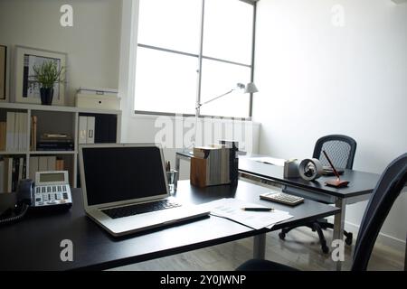 Due scrivanie posizionate vicino alla finestra e ai documenti e un personal computer sulla scrivania della libreria in una stanza bianca Foto Stock