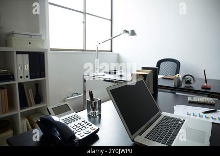 Due scrivanie posizionate vicino alla finestra e ai documenti, un personal computer e una tazza di caffè sulla scrivania della libreria in una camera bianca Foto Stock