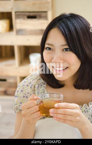 Donna sorridente mentre tiene in mano una tazza di tè Foto Stock