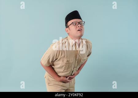 Malata malata, malata, l'impiegato del governo indonesiano in uniforme cachi sta tenendo lo stomaco, sembra scomodo e soffre. Concetto di funzionario pubblico PNS. Foto Stock