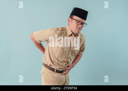 Malata malata, malata, l'impiegato del governo indonesiano in uniforme cachi sta tenendo lo stomaco, sembra scomodo e soffre. Concetto di funzionario pubblico PNS. Foto Stock