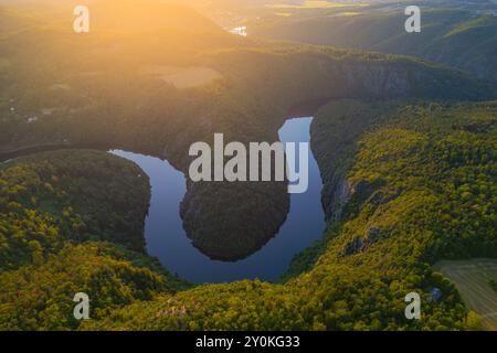 Il fiume Moldava scorre graziosamente attraverso lussureggianti paesaggi verdi in Cechia durante una calda serata estiva, creando pittoreschi meandri. La luce del sole si riflette sull'acqua. Foto Stock