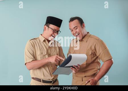 Due felici lavoratori del governo indonesiano che indossano l'uniforme cachi, che tengono e indicano il documento che detengono. PNS e concetto di funzionario pubblico. Foto Stock