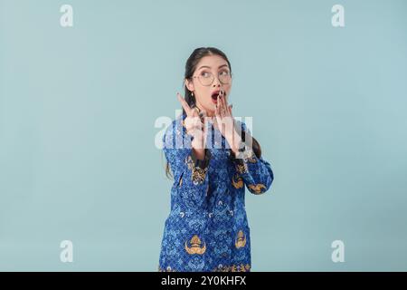Ha sorpreso una donna operaia del governo in uniforme blu batik e occhiali che indicano lo spazio di copia dietro di lei. Concetto di funzionario pubblico PNS. Foto Stock
