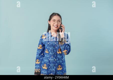Lavoratrice governativa impegnata in uniforme blu batik e occhiali che hanno una chiamata di lavoro. Concetto di funzionario pubblico PNS. Foto Stock