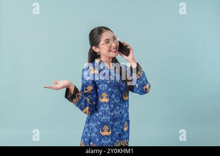 Lavoratrice governativa impegnata in uniforme blu batik e occhiali che hanno una chiamata di lavoro. Concetto di funzionario pubblico PNS. Foto Stock