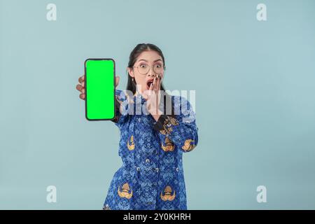 Ha scioccato una donna operaia del governo in uniforme blu batik e occhiali che presentavano spazio di copia sul suo smartphone. Concetto di funzionario pubblico PNS. Foto Stock