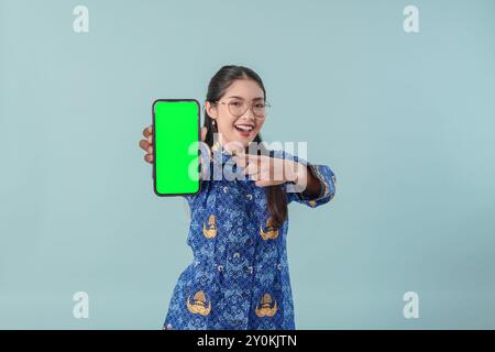 Gioiosa lavoratrice governativa indonesiana che indossa uniforme blu batik e occhiali che puntano a copiare lo spazio sul suo telefono. Concetto di funzionario pubblico PNS. Foto Stock