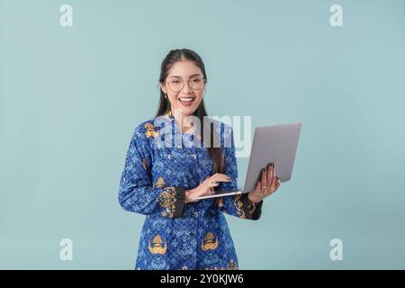 Felice lavoratrice del governo indonesiano che tiene il suo laptop e sorride alla fotocamera. Concetto di funzionario pubblico PNS. Foto Stock