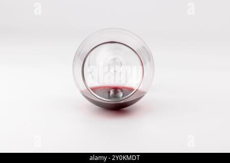 shot verticale di un bicchiere di vino contenente una piccola quantità di vino, collocato sul pavimento bianco. Il vetro è ben visibile sul lato sinistro del Foto Stock