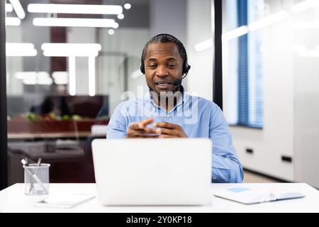 Un uomo d'affari che indossa le cuffie partecipa alle riunioni online. Sedersi alla scrivania con un computer portatile e impegnarsi in comunicazioni professionali. Concentrati sulle discussioni di lavoro Foto Stock