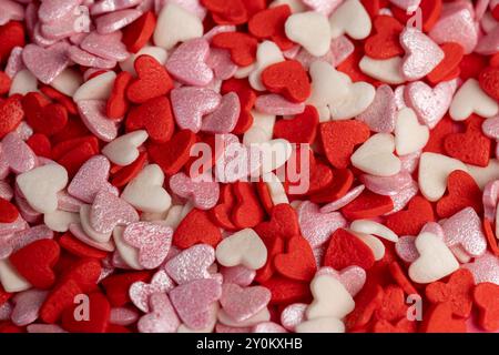 caramelle rosse, bianche e rosa sparse su carta rossa, caramelle a forma di cuore vengono utilizzate per decorare le torte Foto Stock