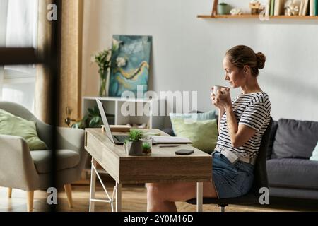 La donna sorride mentre sorseggia un caffè in uno spazio di lavoro luminoso e invitante. Foto Stock