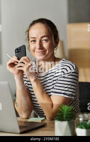 Una bella donna con vitiligine sorride mentre tiene in mano il suo smartphone. Foto Stock