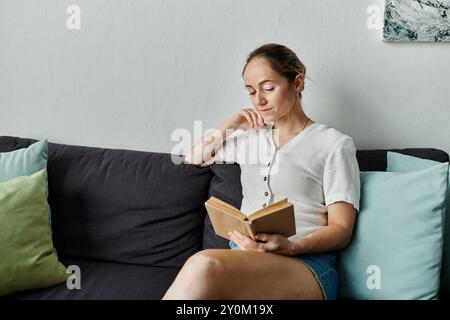 Una giovane donna premurosa ama un libro mentre si rilassa su un morbido divano. Foto Stock