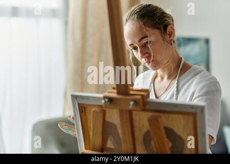 Una donna di talento con vitiligine si concentra intensamente sulla sua tela mentre dipinge. Foto Stock