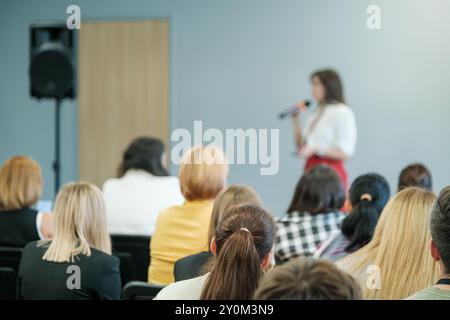 Donna d'affari che fa una presentazione a una conferenza. Il pubblico ascolta attentamente in un ambiente aziendale. Opportunità di sviluppo professionale e networking. Foto Stock