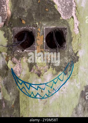 Primo piano di pareti intemprate con faccia sorridente dipinta con due prese vuote che ricordano gli occhi. Arte strutturata e astratta nel paesaggio urbano. Foto Stock