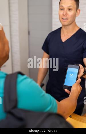 Pagare con smartphone, medico maschile o operatore sanitario in scrub, paziente visita clinica medica Foto Stock