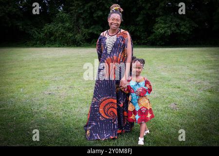 Una giovane madre e venditore all'annuale Wakanda Celebration che indossa distintivi abiti dell'Africa occidentale. Con sua figlia a Mount Vernon, Westchester. Foto Stock