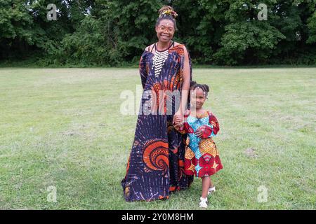 Una giovane madre e venditore all'annuale Wakanda Celebration che indossa distintivi abiti dell'Africa occidentale. Con sua figlia a Mount Vernon, Westchester. Foto Stock