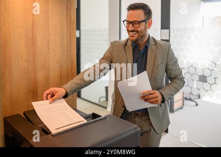 Ritratto di una tipografia sorridente maschile che sorride e che mette un foglio di carta nella fotocopiatrice in ufficio Foto Stock