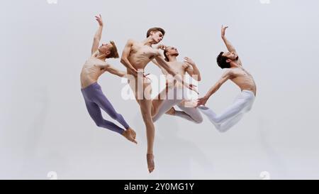 Quattro ballerini saltano all'unisono, i loro corpi creano una potente visuale di forza e grazia attraverso un allenamento rigoroso su sfondo bianco in studio. Foto Stock