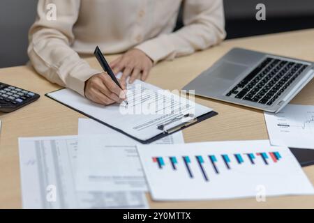 Donna d'affari ispanica alla scrivania dell'ufficio che analizza documenti finanziari con laptop e calcolatrice. Mani che prendono appunti, concentrandosi sulle prestazioni aziendali. Foto Stock