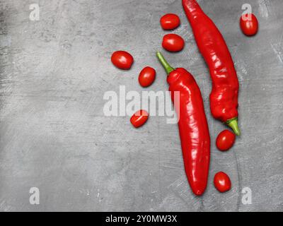 Peperoncino rosso caldo e pomodori ciliegini su sfondo grigio, vista dall'alto. Concetto gastronomico minimalista. Foto Stock