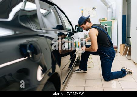 Lavoratore meccanico specializzato maschio nella porta di lucidatura del tappo di un'auto di lusso in un'officina di riparazione che utilizza una lucidatrice orbitale. Tecnico esperto di verniciatura per auto che utilizza Foto Stock