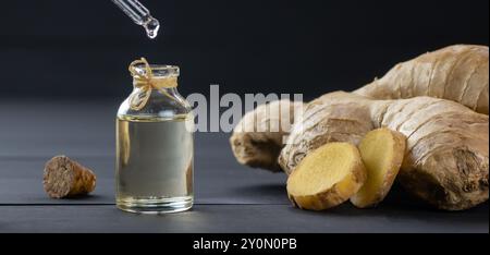 Bottiglia in vetro di olio essenziale di zenzero, radice di zenzero e polvere su fondo rustico in legno nero, gocciolamento di olio, Zingiber officinale Foto Stock