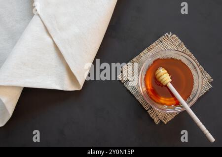Pezzo di miele liquido organico fresco a nido d'ape in ciotola di vetro con cucchiaio su fondo rustico, cibo sano Foto Stock
