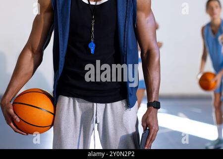 Regge la pallacanestro, coach con fischio in palestra con i giocatori sullo sfondo Foto Stock