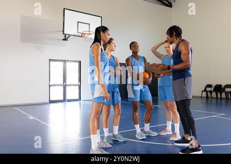 Allenatore maschile di pallacanestro che discute di strategia con le giocatrici di squadra femminili in palestra Foto Stock