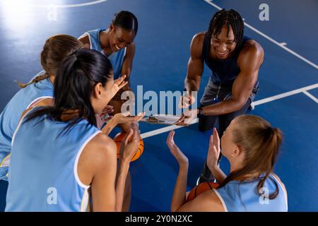 Allenatore maschile di pallacanestro che discute strategia con le giocatrici di squadra femminili sul campo Foto Stock