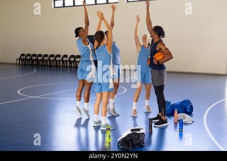 Squadra di pallacanestro che pratica in palestra, allenatore maschile che tiene la palla e dà istruzioni Foto Stock