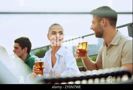 Il giovane barbuto si diverte con una birra fredda in un ambiente rilassato all'aperto, assaporando momenti indimenticabili. Una donna siede qui vicino. Atmosfera festosa. Foto Stock