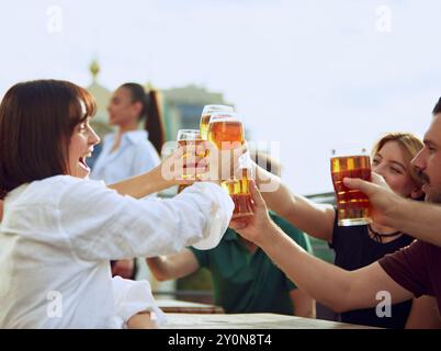 Gli amici si riuniscono intorno al tavolo, alzando i bicchieri con un brindisi per passare i momenti migliori. L'atmosfera vivace e le risate condivise rendono perfetta la giornata di sole. Foto Stock