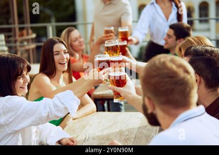 Gli amici si riuniscono intorno al tavolo, alzando i bicchieri con un brindisi per passare i momenti migliori. L'atmosfera vivace e le risate condivise rendono perfetta la giornata di sole. Foto Stock