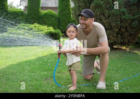 Padre e suo figlio innaffiano il prato con il tubo nel cortile Foto Stock