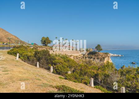 Case sulla scogliera con vista sull'oceano e alte palme sotto un cielo azzurro. Foto Stock