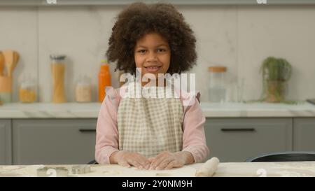 Ritratto felice sorridente piccola ragazza afroamericana in grembiule solo sorriso bambino positivo figlia etnica in posa vicino a tavola cuoco cottura in cottura Foto Stock